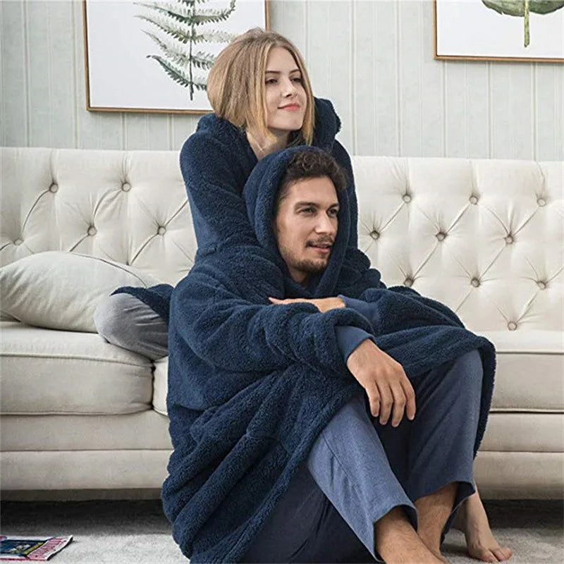 Two people sitting on a couch under a blue blanket in a living room setting.